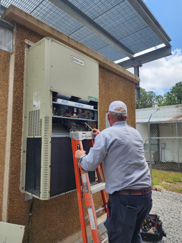 A technician inspecting an HVAC unit on a transmitter building.